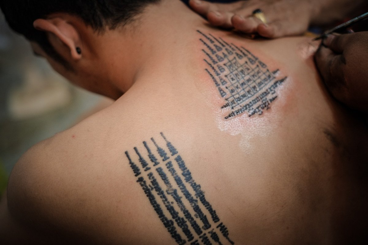 A master monk applying a sacred Sak Yant tattoo by hand onto a man's back in a traditional Thai temple